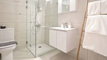 Un baño moderno con cabina de ducha de vidrio, un lavamanos blanco y un inodoro.