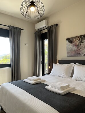 A hotel room with a large bed, grey curtains, a ceiling fan, an air conditioning unit, and a painting on the wall. - Aellō luxury apartments (Markopoulo Mesogaias)