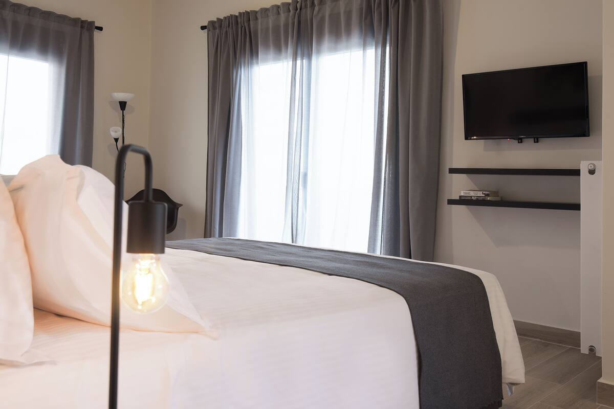 A hotel room with a bed, a TV mounted on the wall, and a window with curtains.