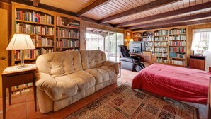 A cozy room with a large beige sofa, a red bed, and extensive bookshelves filled with books. - Southern California Vacation Rental: Private Pool! (Ontario)