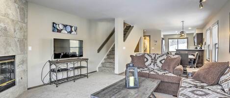 Una sala de estar moderna con chimenea, televisor y una escalera que lleva a un comedor.