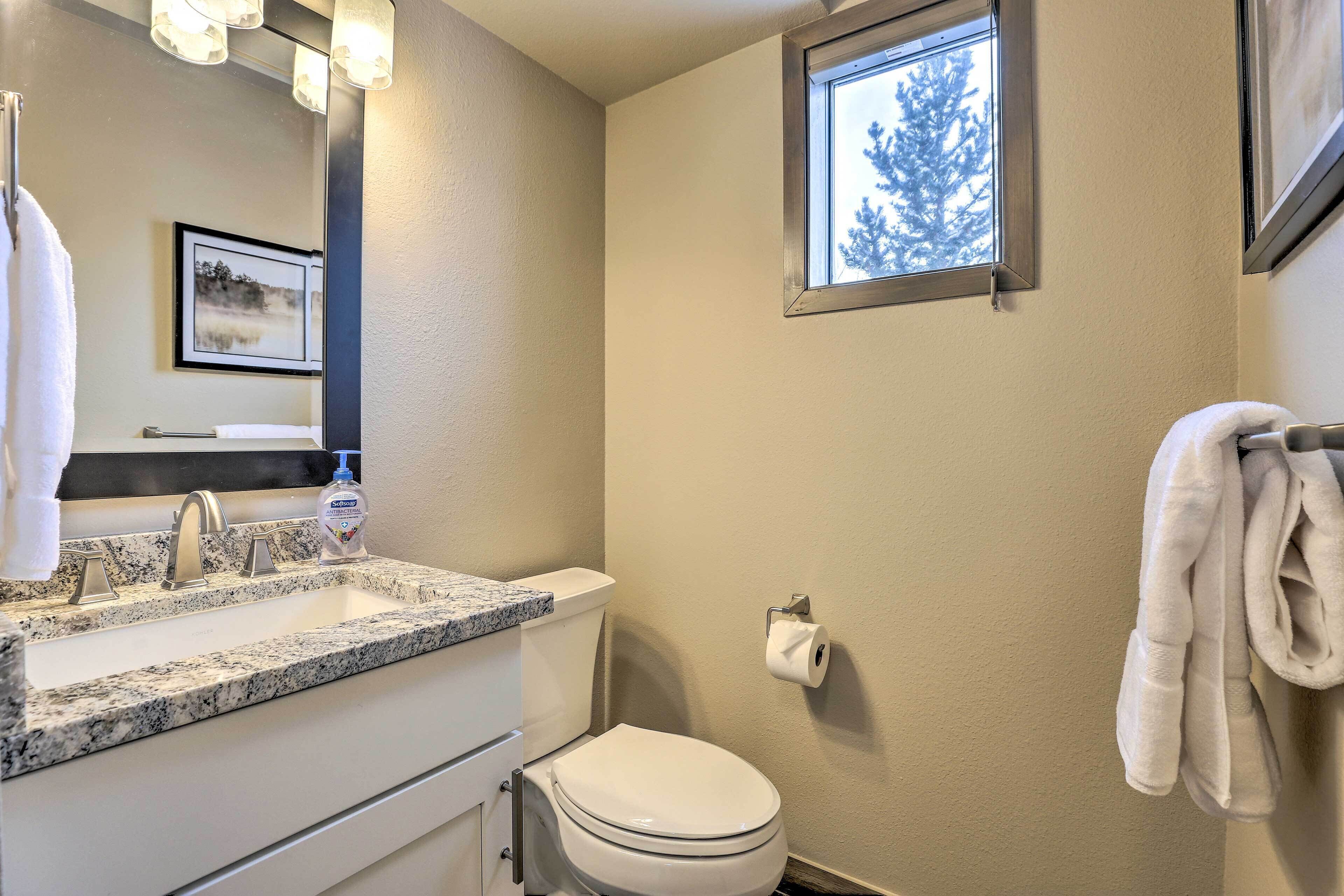 Een badkamer met een wastafel met granieten blad, een toilet, een handdoekhouder en een raam met uitzicht op bomen.