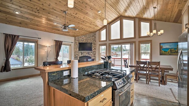 A modern kitchen with granite countertops, a gas stove, and a large island. There is a dining area with wooden furniture and a stone fireplace. - 9 Mi to Heavenly Mountain: South Lake Tahoe Home! (South Lake Tahoe)