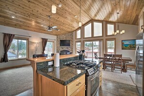 Une cuisine moderne dotée de plans de travail en granit, d’une cuisinière à gaz et d’un grand îlot central. On y trouve également un coin repas avec des meubles en bois et une cheminée en pierre.