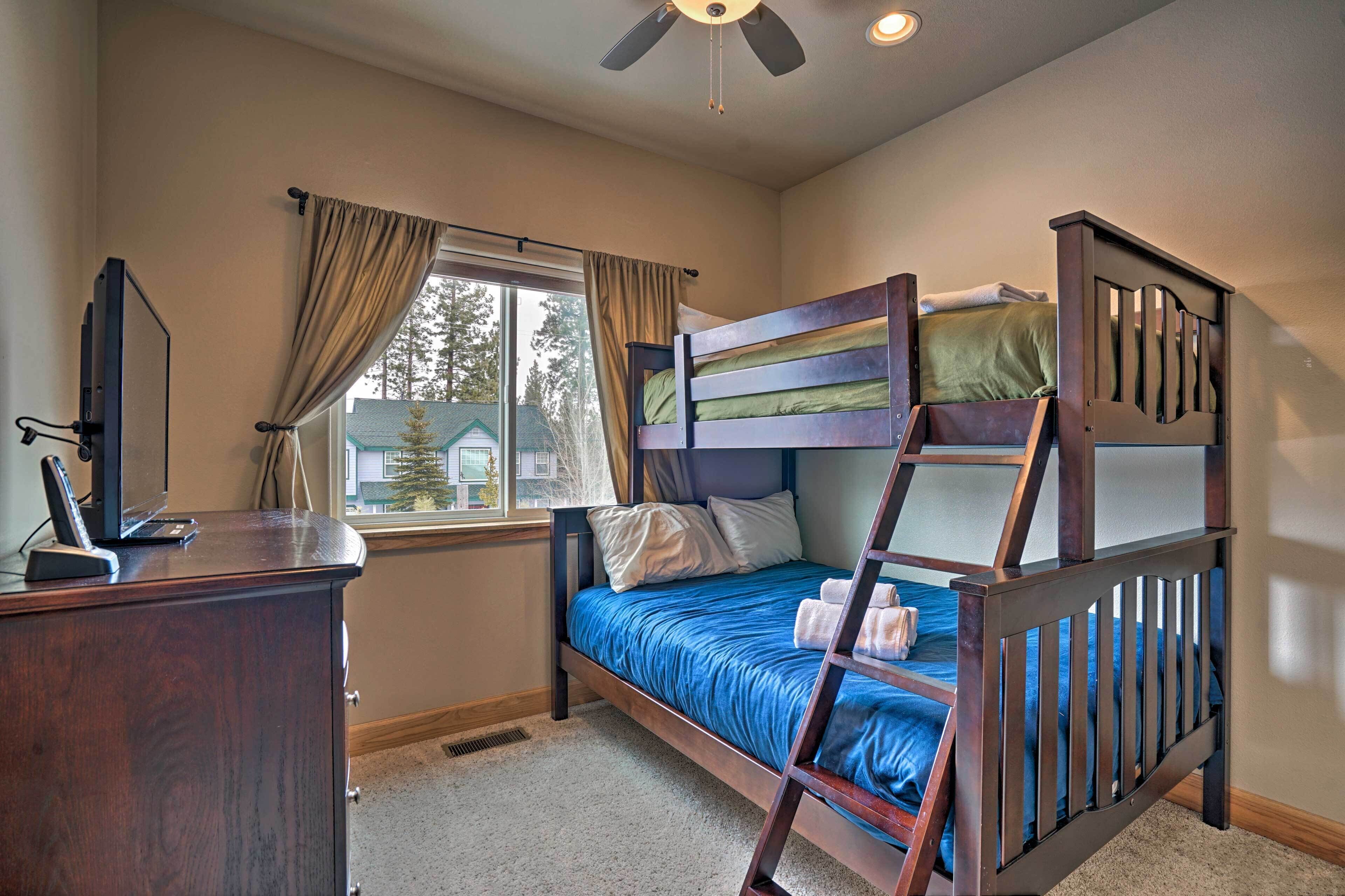 A bedroom with a bunk bed, a desk with a computer, a window with curtains, and a ceiling fan.