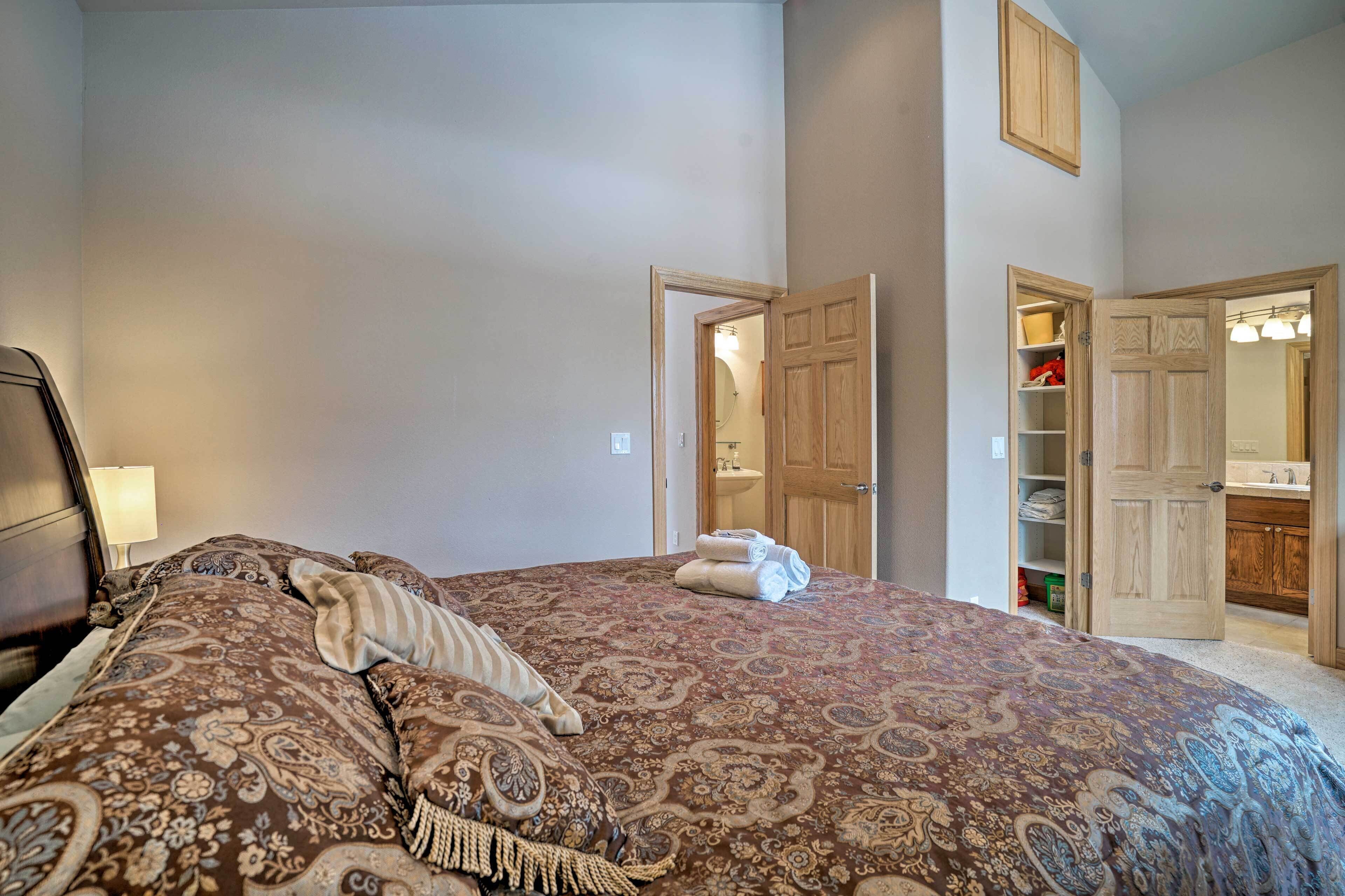 A bedroom with a large bed, a nightstand, a wooden wardrobe, and an open door leading to a bathroom.