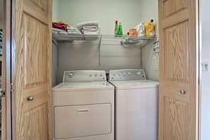 A laundry area with two front-loading washing machines, a metal shelf above holding towels and cleaning supplies, and wooden doors. - 9 Mi to Heavenly Mountain: South Lake Tahoe Home! (South Lake Tahoe)