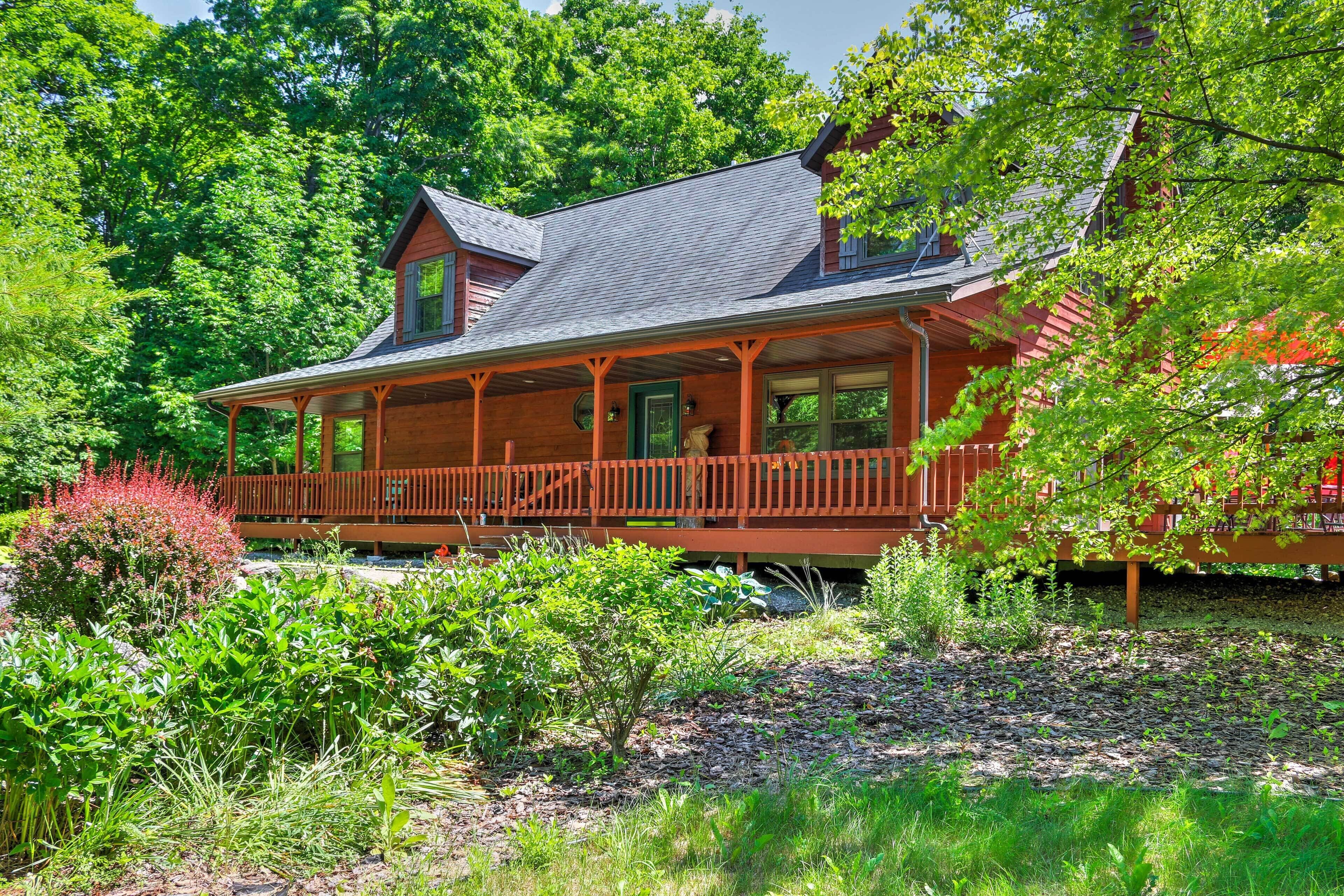 A wooden house with a porch, surrounded by lush greenery and trees.
