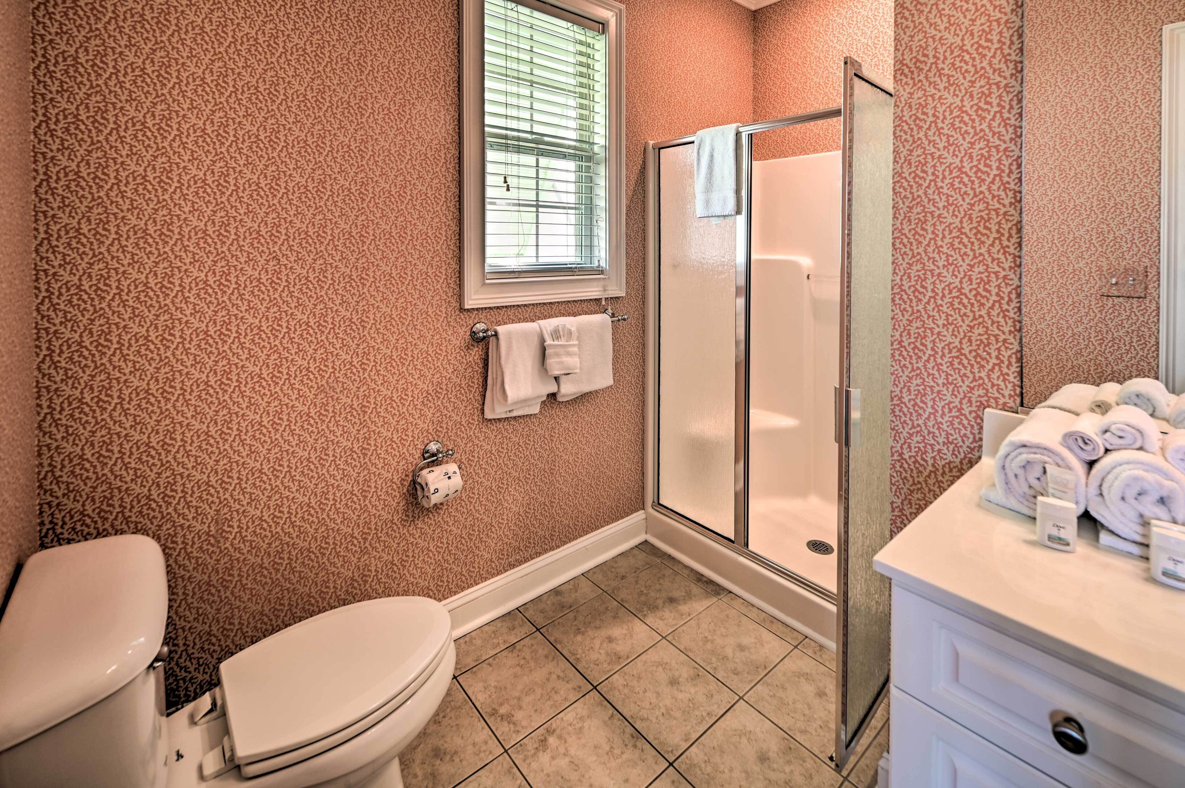 Een badkamer met een luipaardprint behang, een toilet, een douche met glazen deur en een wastafel met handdoeken.