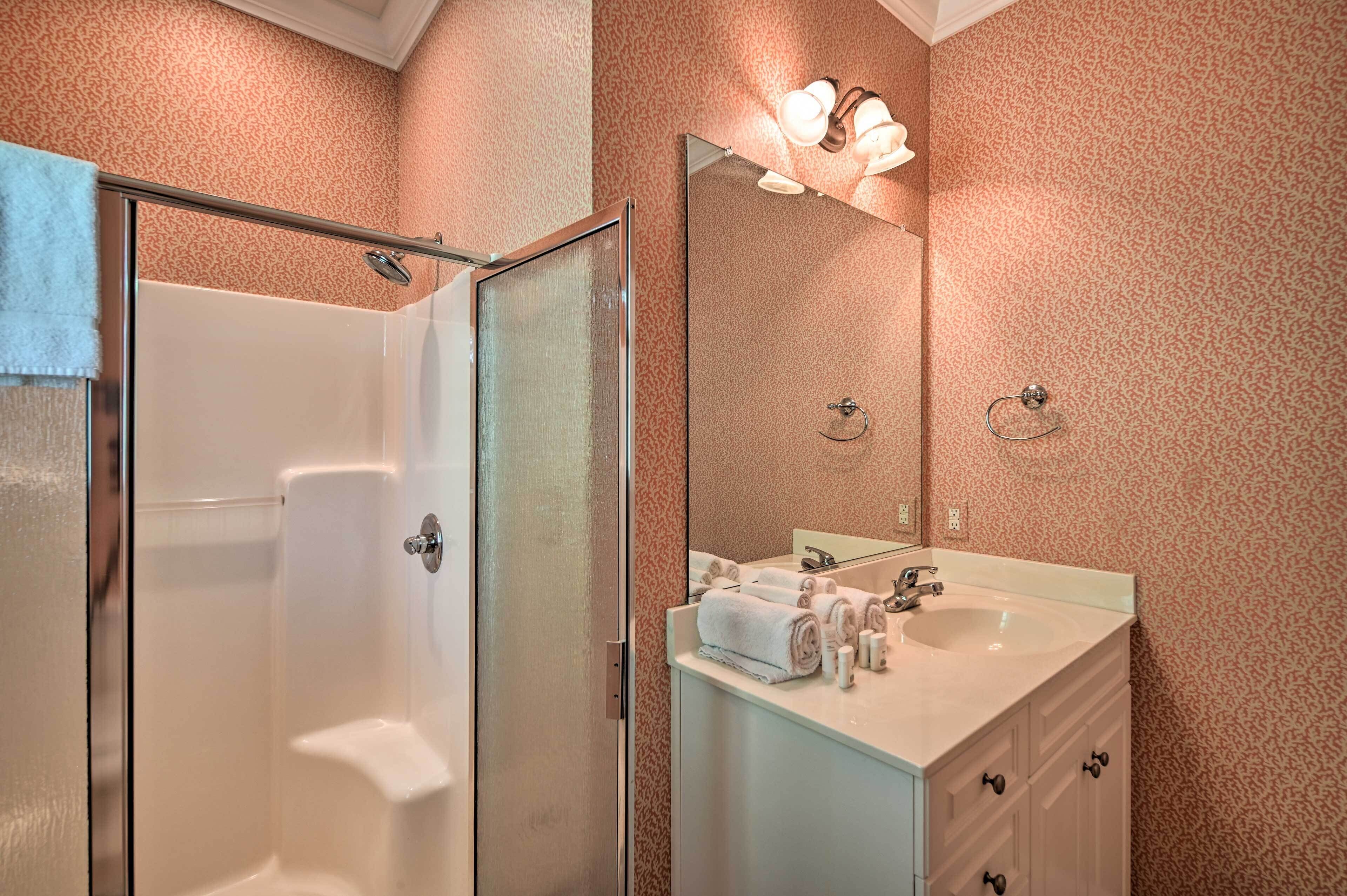 A bathroom with a glass shower door, a sink with toiletries, and a mirror with lights.
