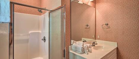A bathroom with a glass shower door, a sink with toiletries, and a mirror with lights.