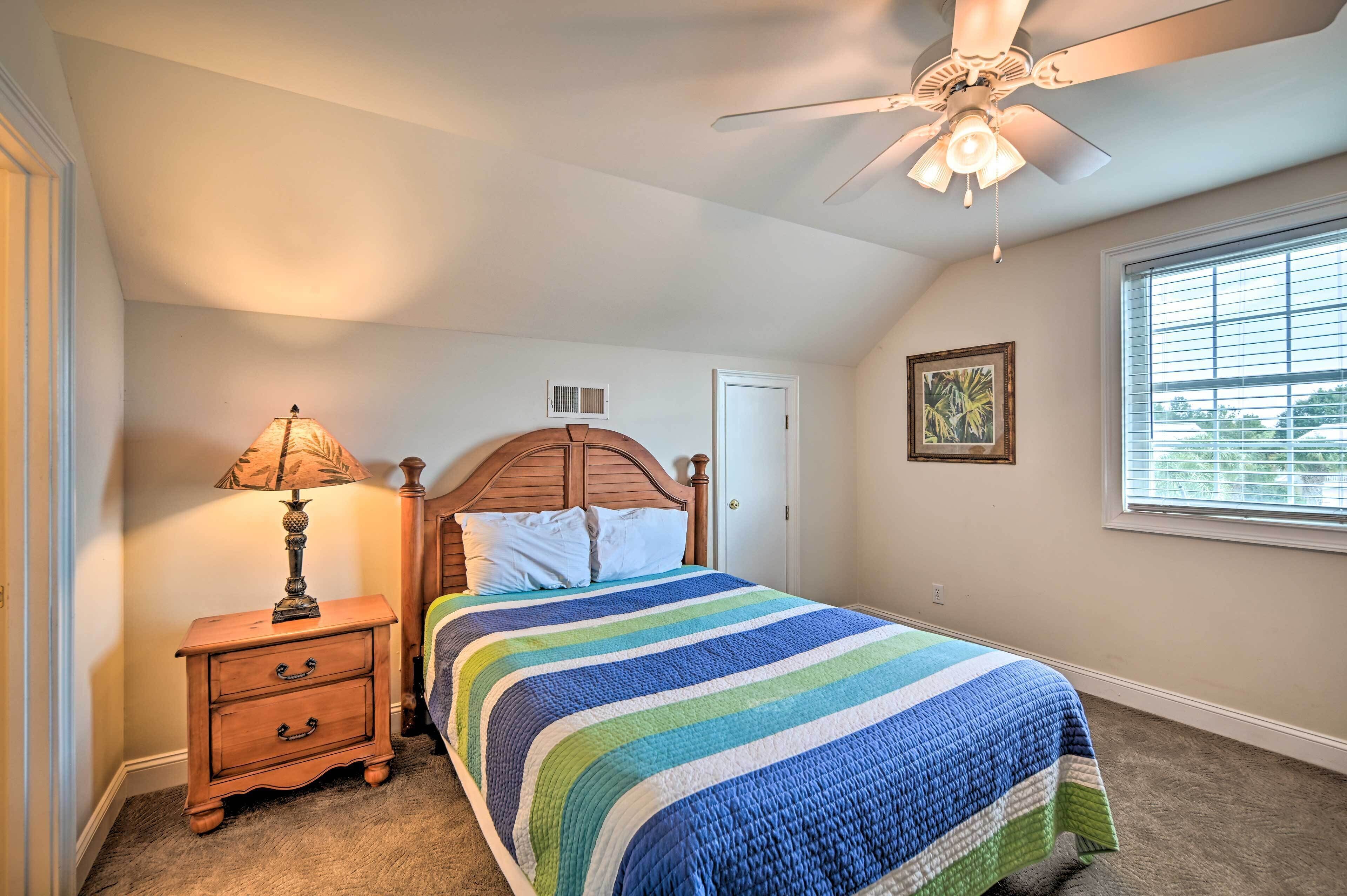 A bedroom with a bed, a nightstand, a ceiling fan, a window, and a door.