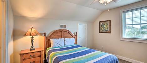 A bedroom with a bed, a nightstand, a ceiling fan, a window, and a door.