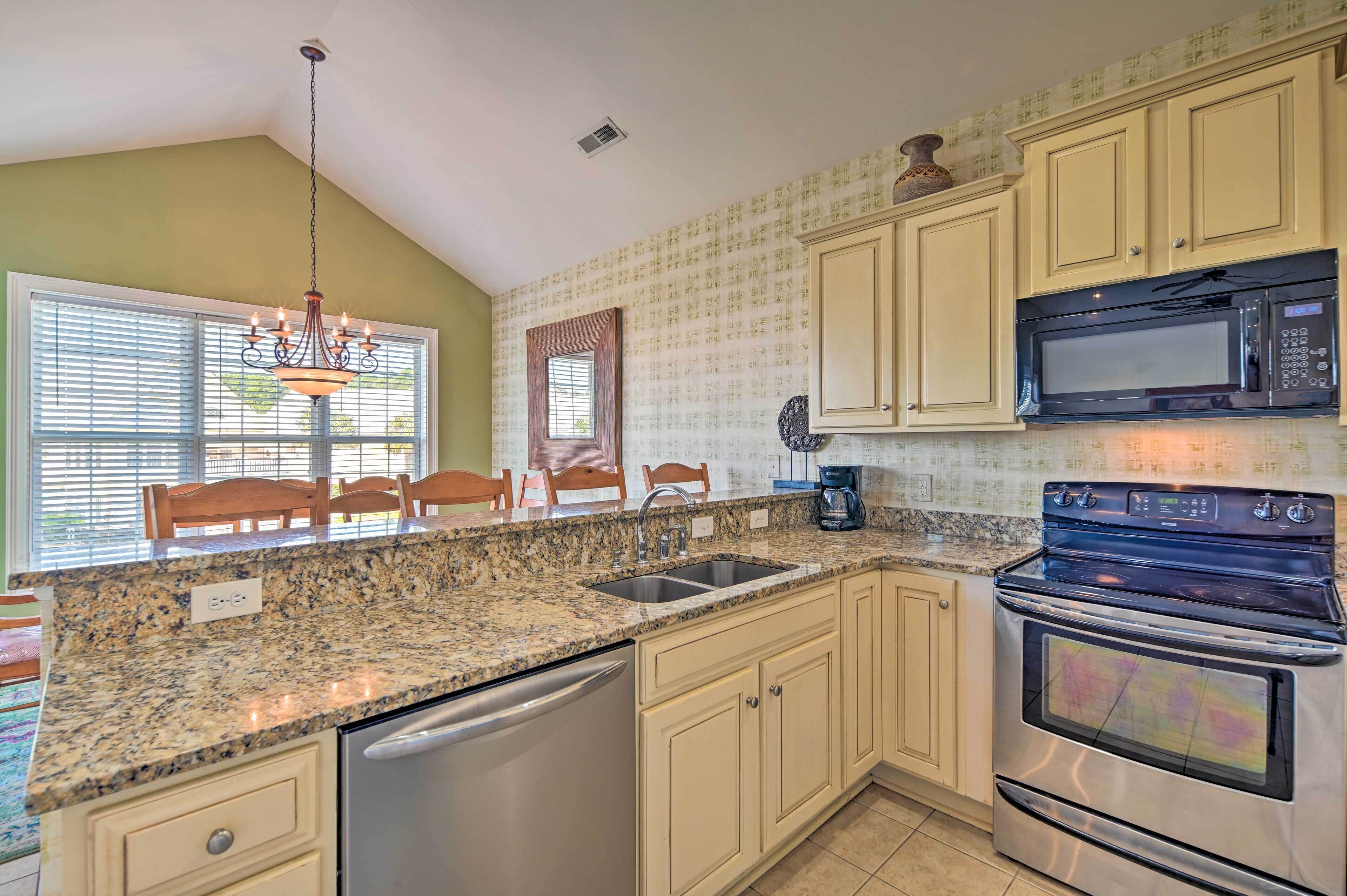 A kitchen with granite countertops, a stainless steel dishwasher, a built-in oven, a microwave, and wooden chairs.