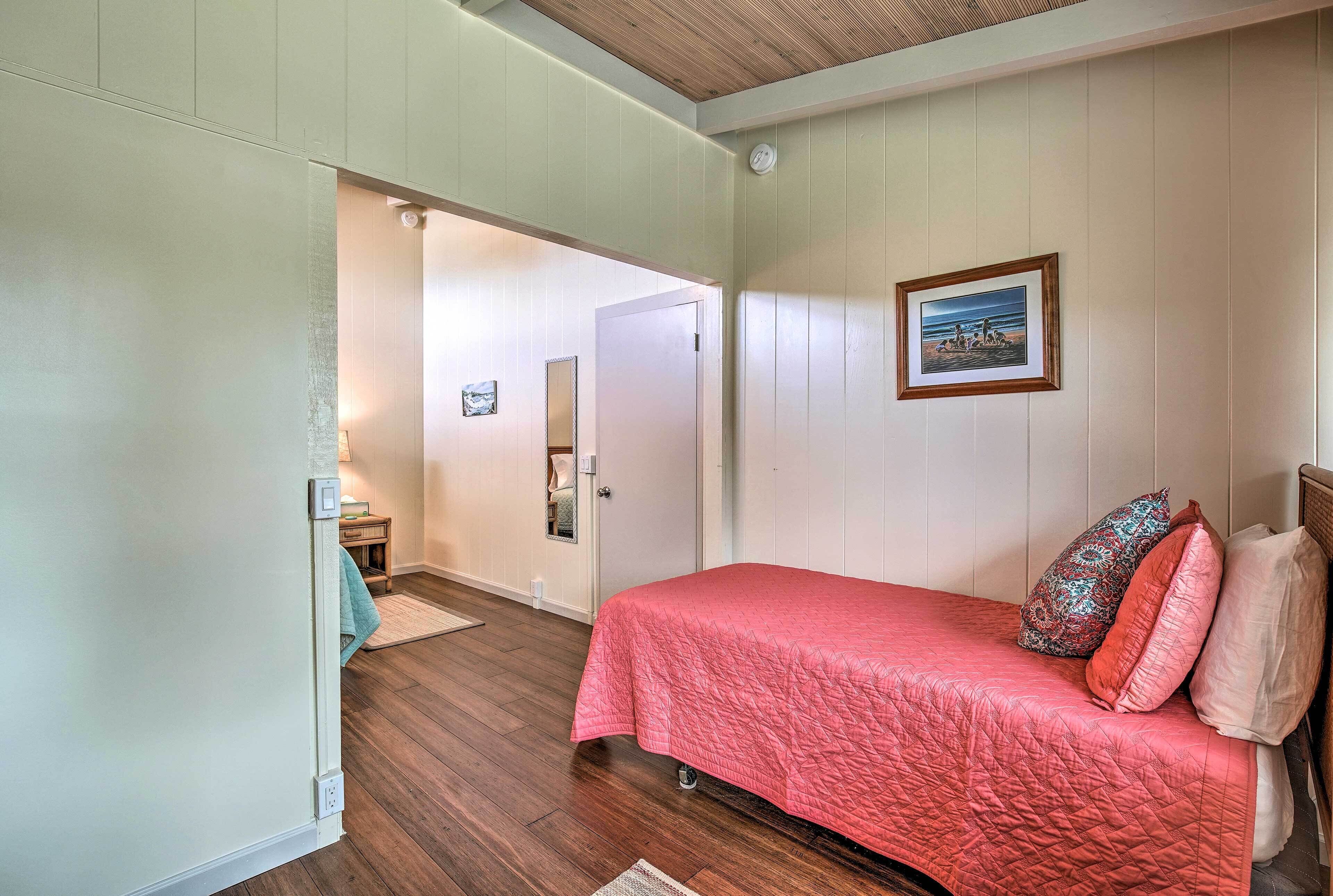 A bedroom with a bed, a door, a framed picture, and a light switch on the wall.