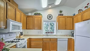 Una cocina con armarios de madera, una estufa blanca, un refrigerador blanco y una ventana con vistas a árboles.