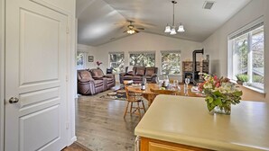Un salón comedor amplio con chimenea, zona de estar con mesa y sillas, y cocina con encimera y un jarrón de flores.