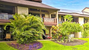 A two-story building with a balcony, a well-maintained lawn, and various plants. - Chic Waikoloa Condo w/ Lanai + Complex Pools! (Waikoloa)