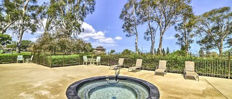 A hot tub surrounded by lounge chairs and a fenced garden area with trees.