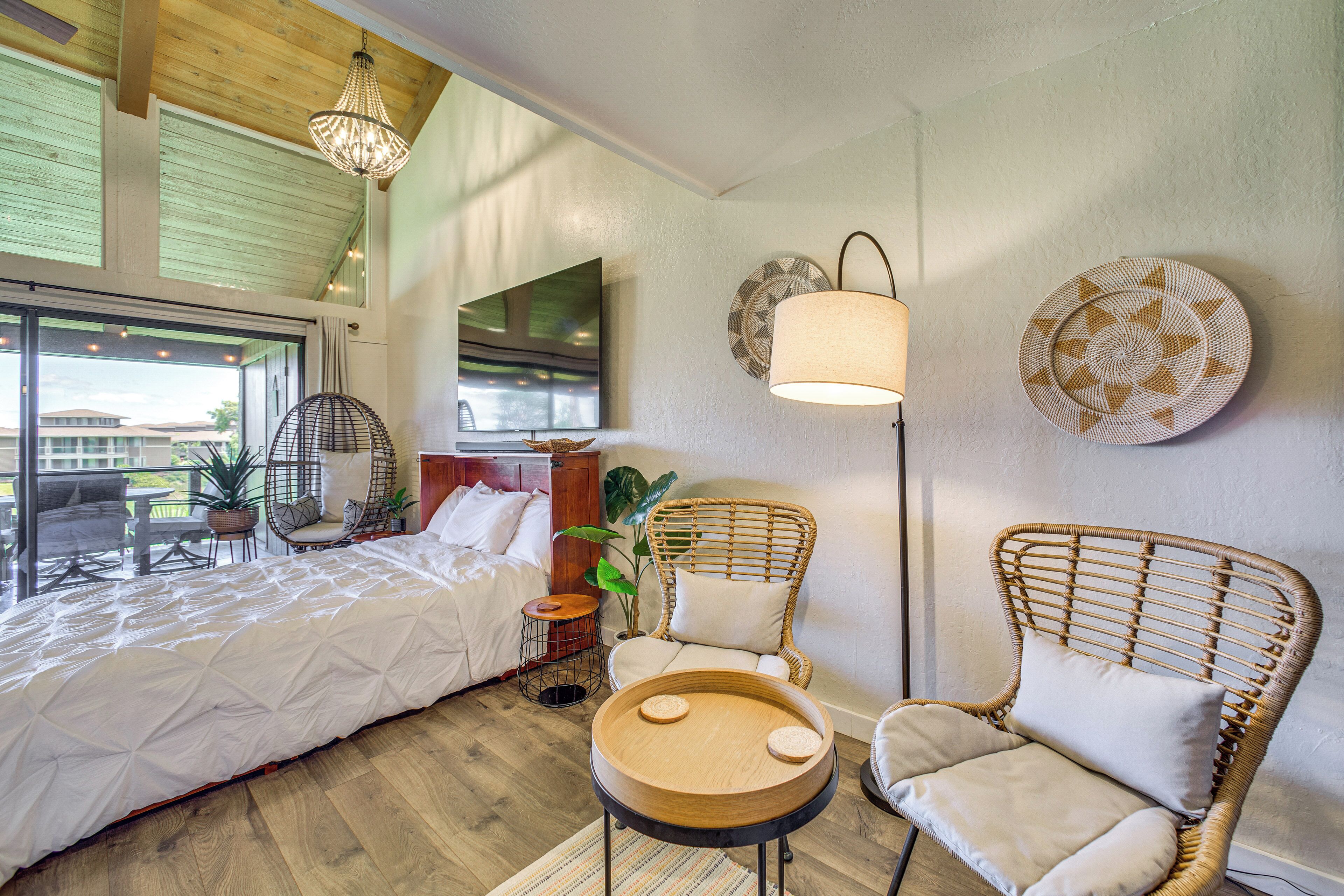 Ein Schlafzimmer mit einem Bett, zwei Korbstühlen, einem kleinen Tisch, einer Stehlampe und einem großen Fenster.