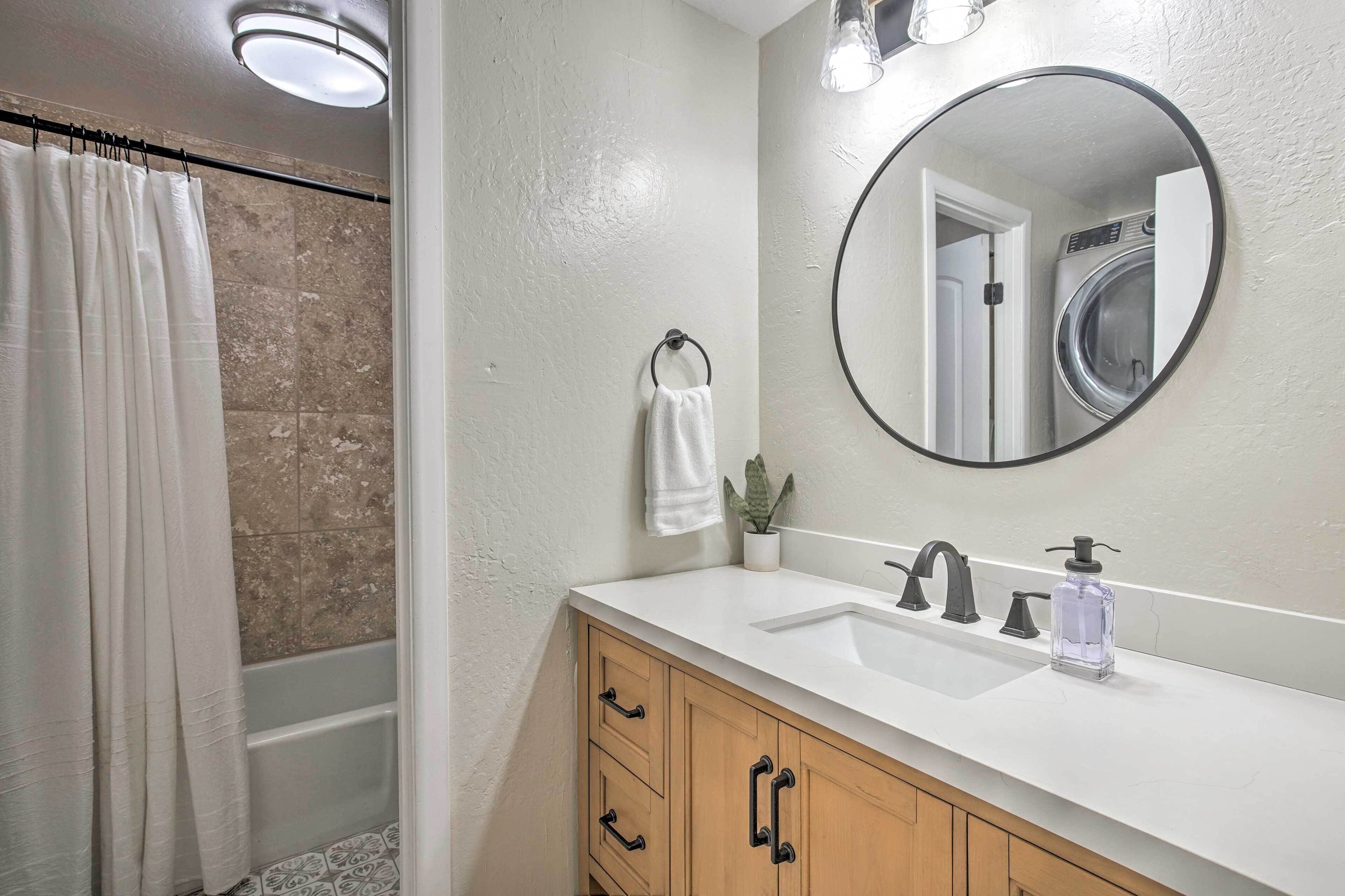 A bathroom with a white sink, a round mirror, a towel ring, and a potted plant.
