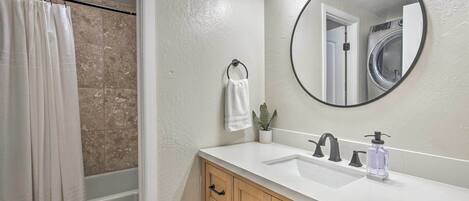 A bathroom with a white sink, a round mirror, a towel ring, and a potted plant.