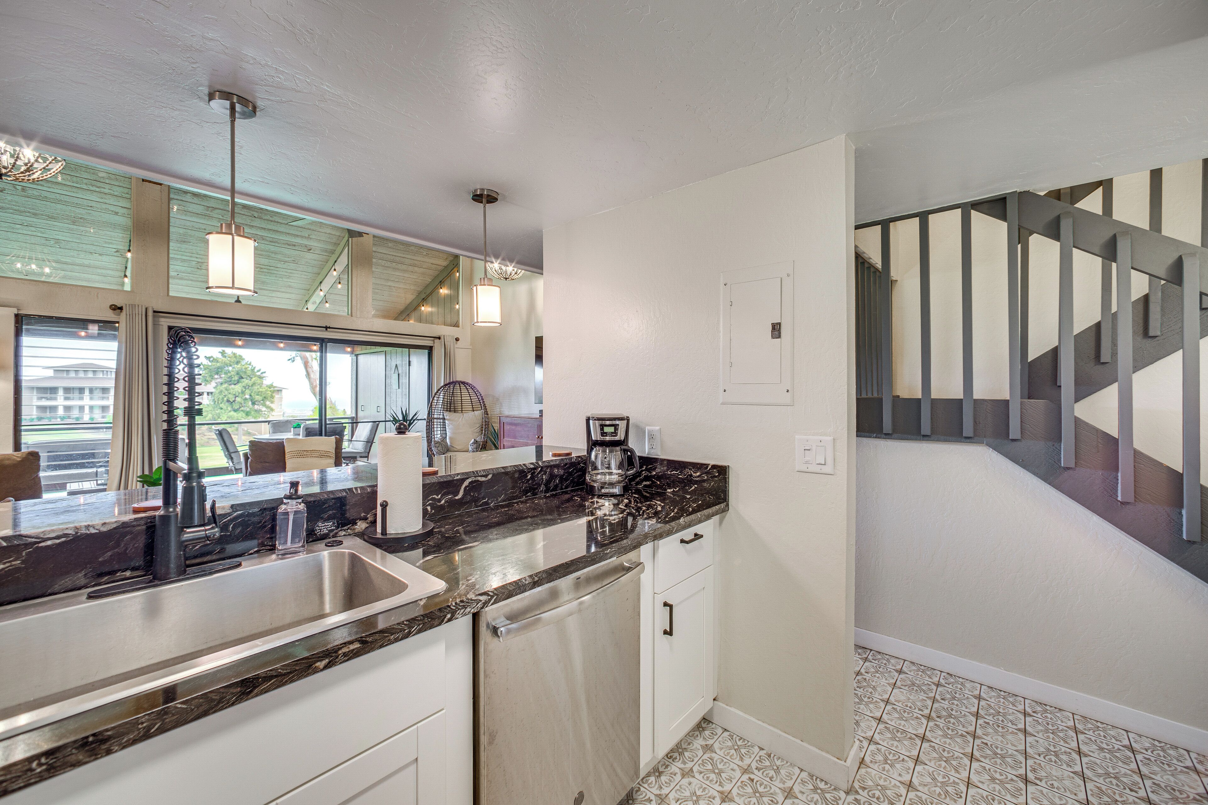 A modern kitchen with a marble countertop, stainless steel sink, and a coffee maker.