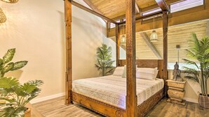 A four-poster bed with a wooden frame and a patterned bedspread, surrounded by potted plants and a view of the outdoors. - Chic Waikoloa Condo w/ Lanai + Complex Pools! (Waikoloa)