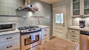 A kitchen with a gas stove, oven, microwave, and a stainless steel range hood. There are white cabinets with glass doors and a wooden countertop. - 3 Mi to Soco: City Escape w/ Patio (Austin)