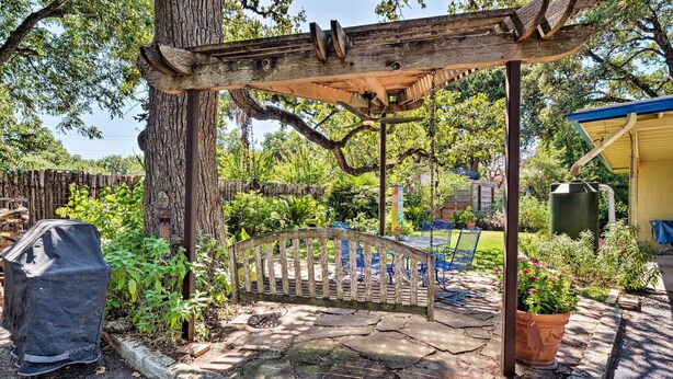 A wooden pergola with a bench, surrounded by a stone patio and lush greenery. - 3 Mi to Soco: City Escape w/ Patio (Austin)