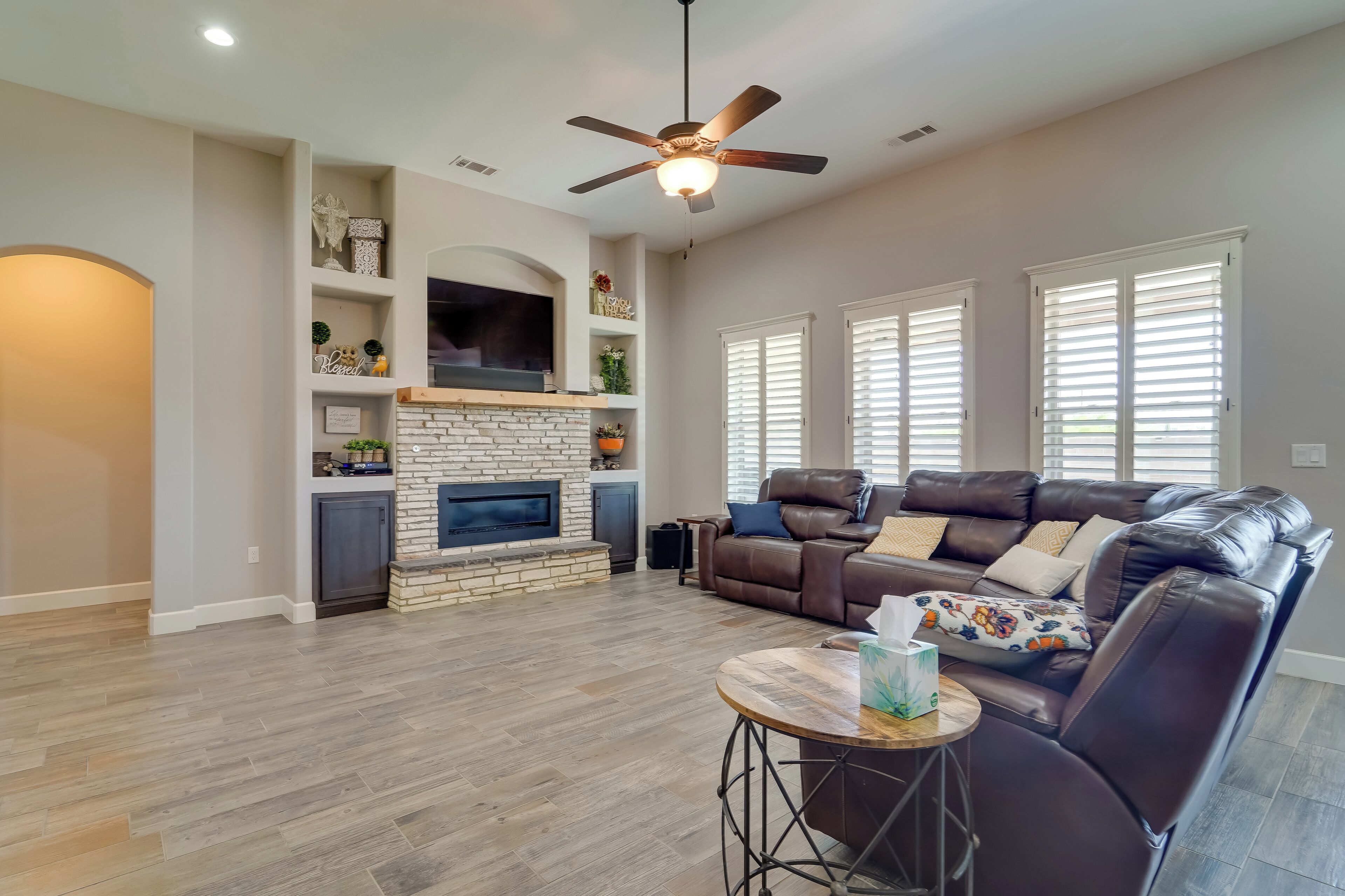 A spacious living room with a fireplace, leather sofa, and a ceiling fan.