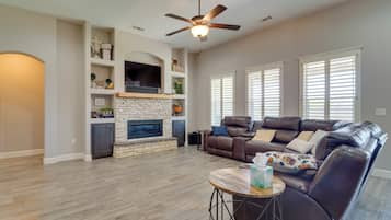 A spacious living room with a fireplace, leather sofa, and a ceiling fan.