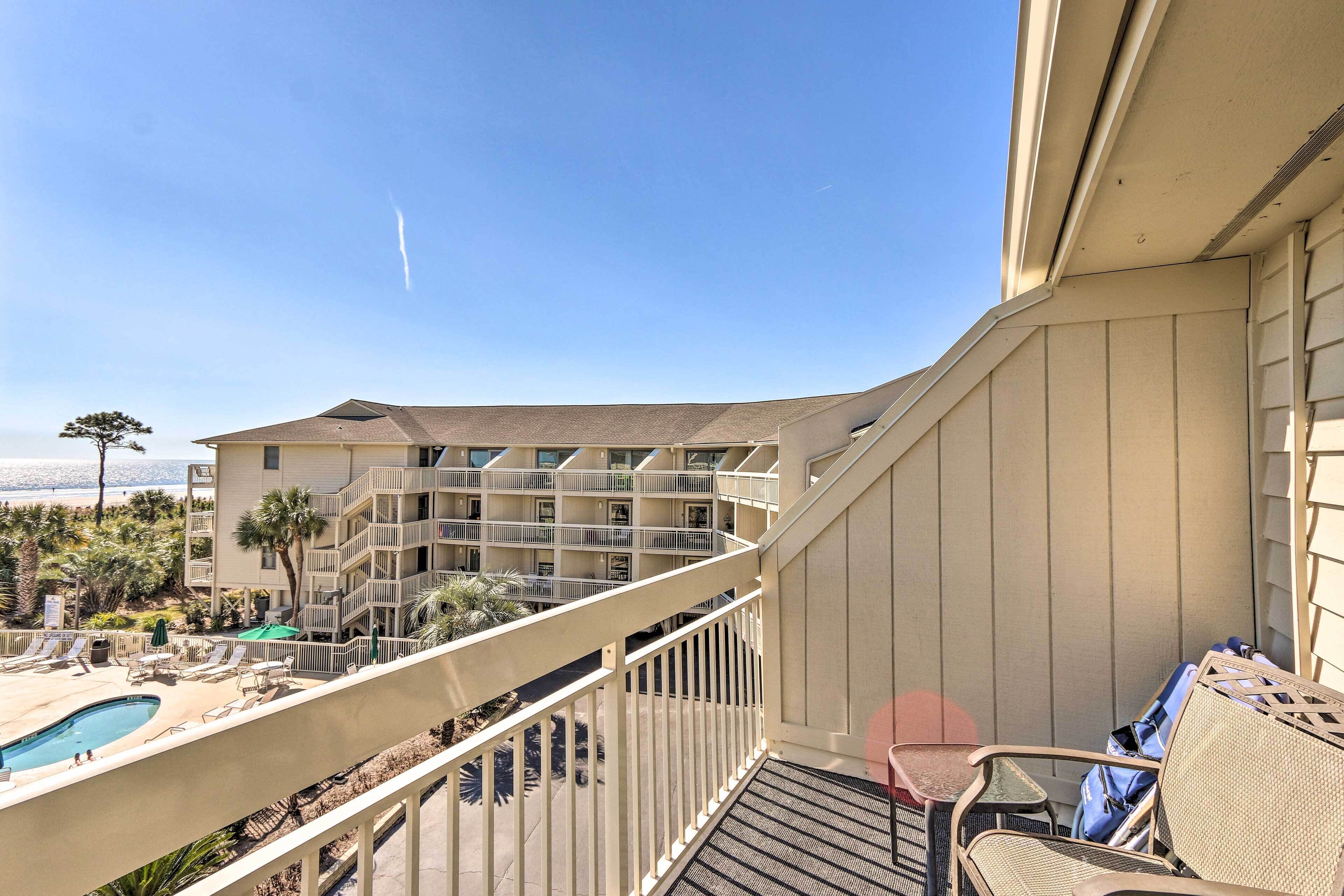 A balcony with a pool, lounge chairs, and a view of a multi-story building.