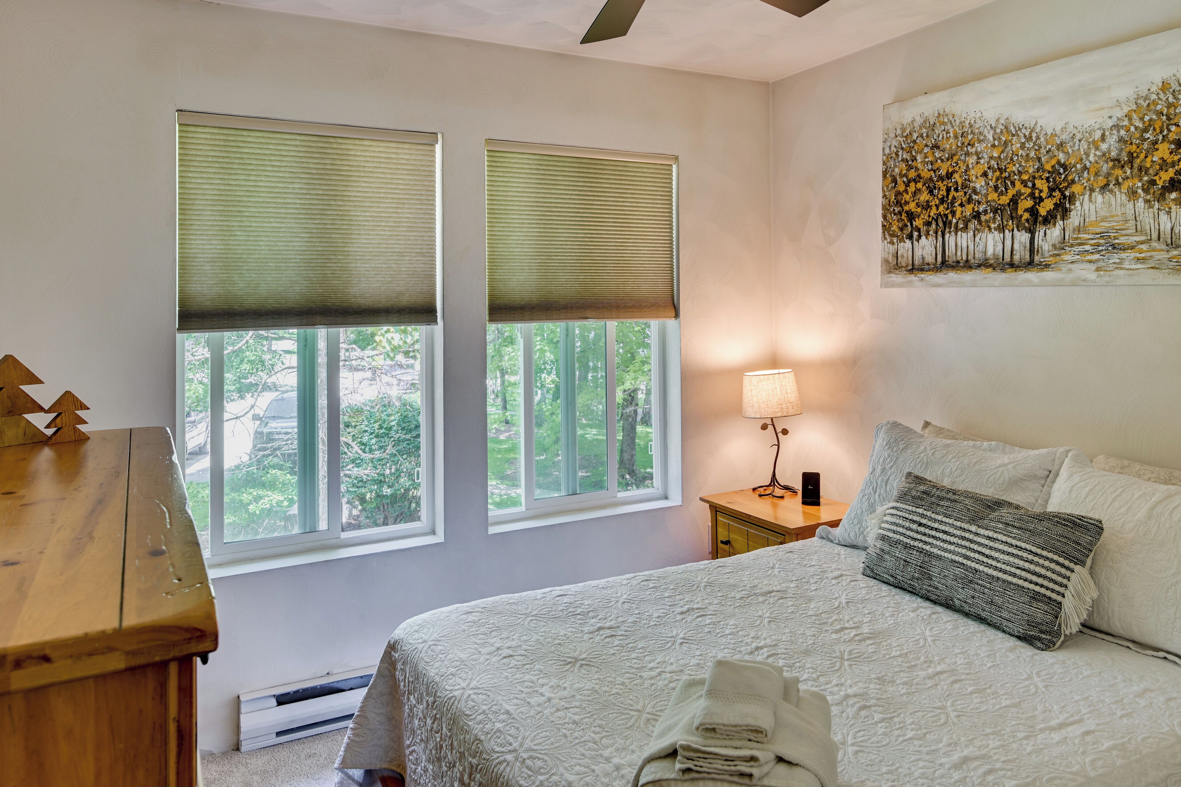 A bedroom with a bed, a nightstand, a lamp, and two windows with blinds.
