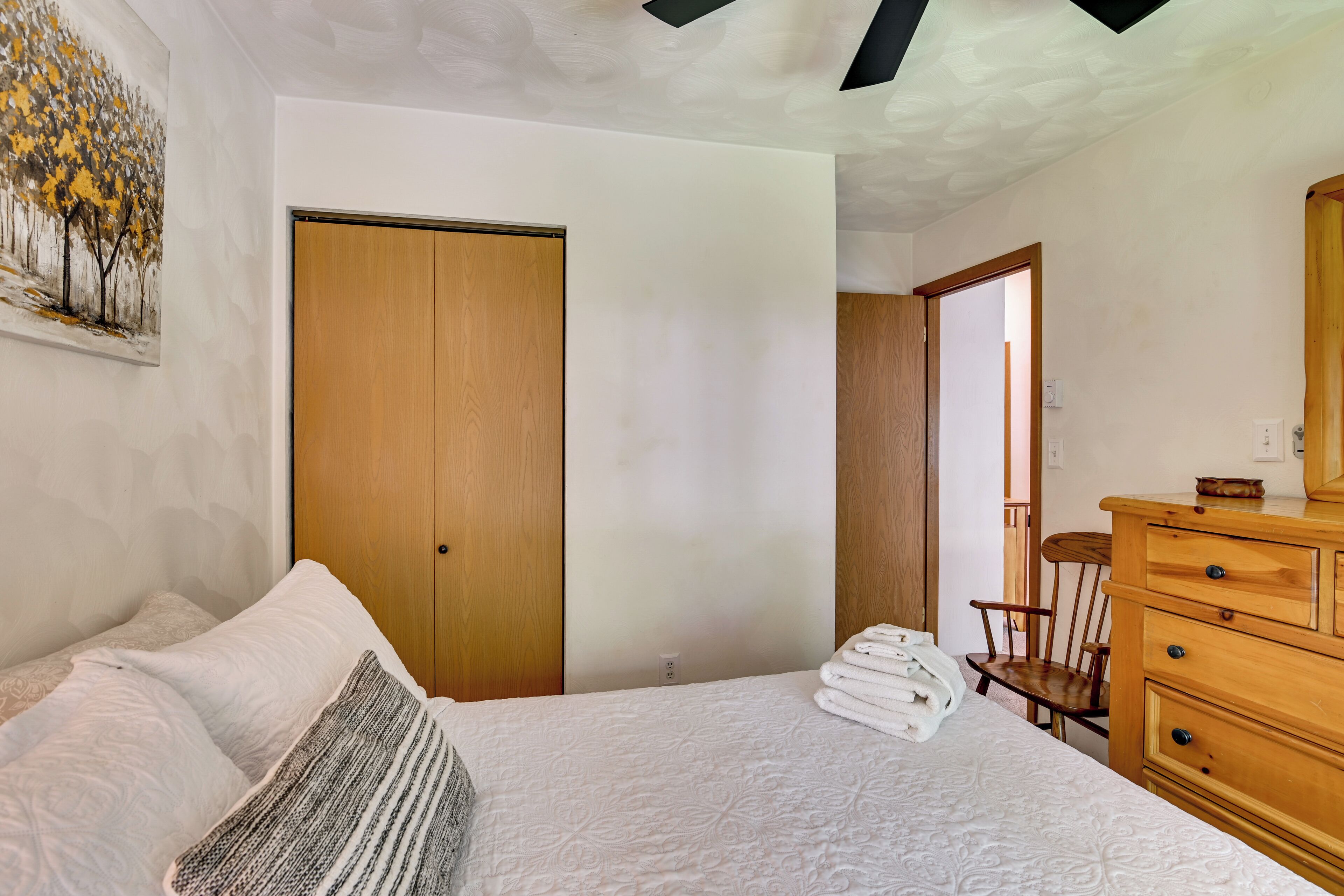 A bedroom with a bed, a wooden dresser, a chair, and a door.