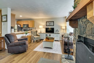 A living room with a fireplace, a television, and a kitchen in the background.