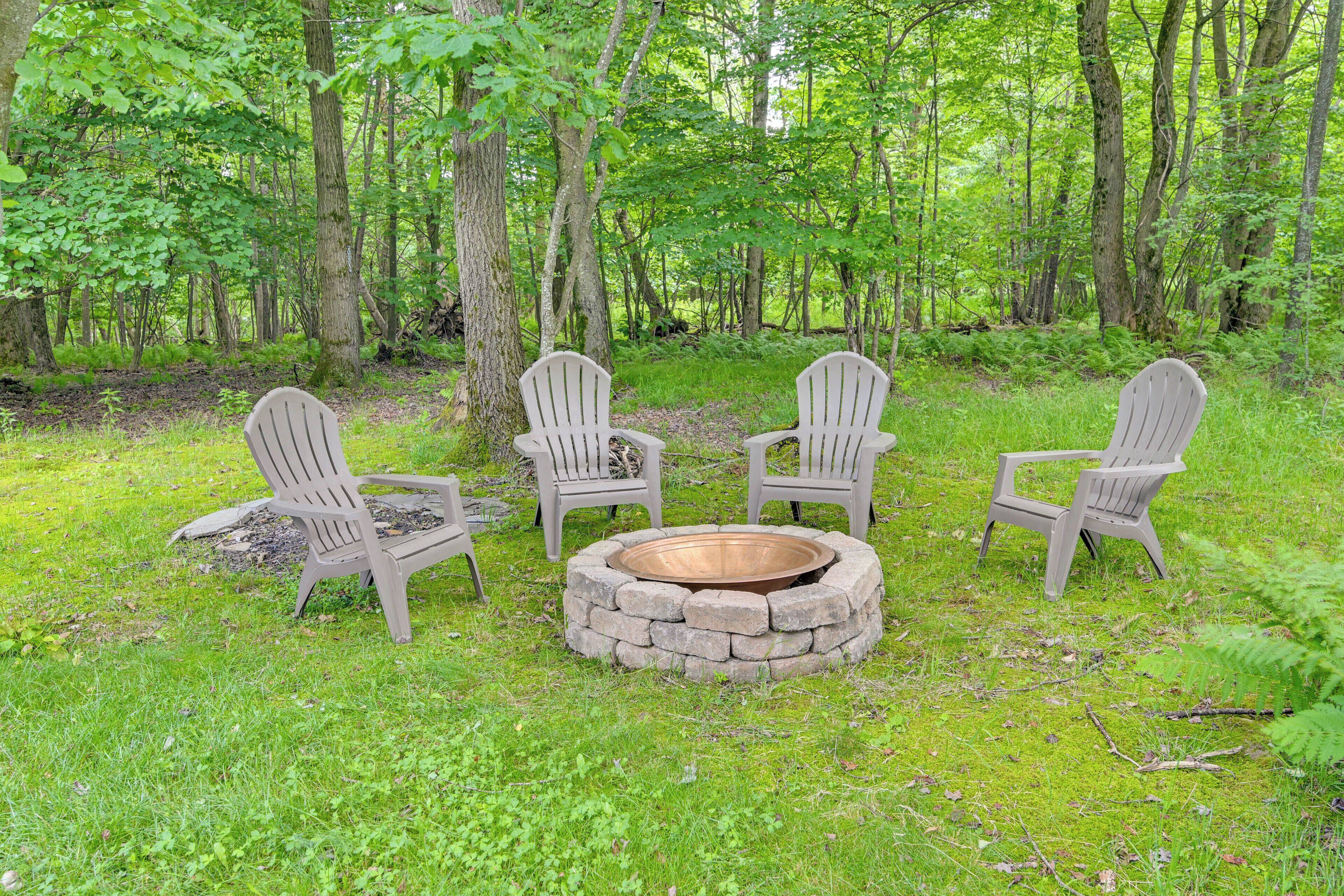 Een ronde vuurplaats van steen met vier Adirondack-stoelen in een bebost gebied.