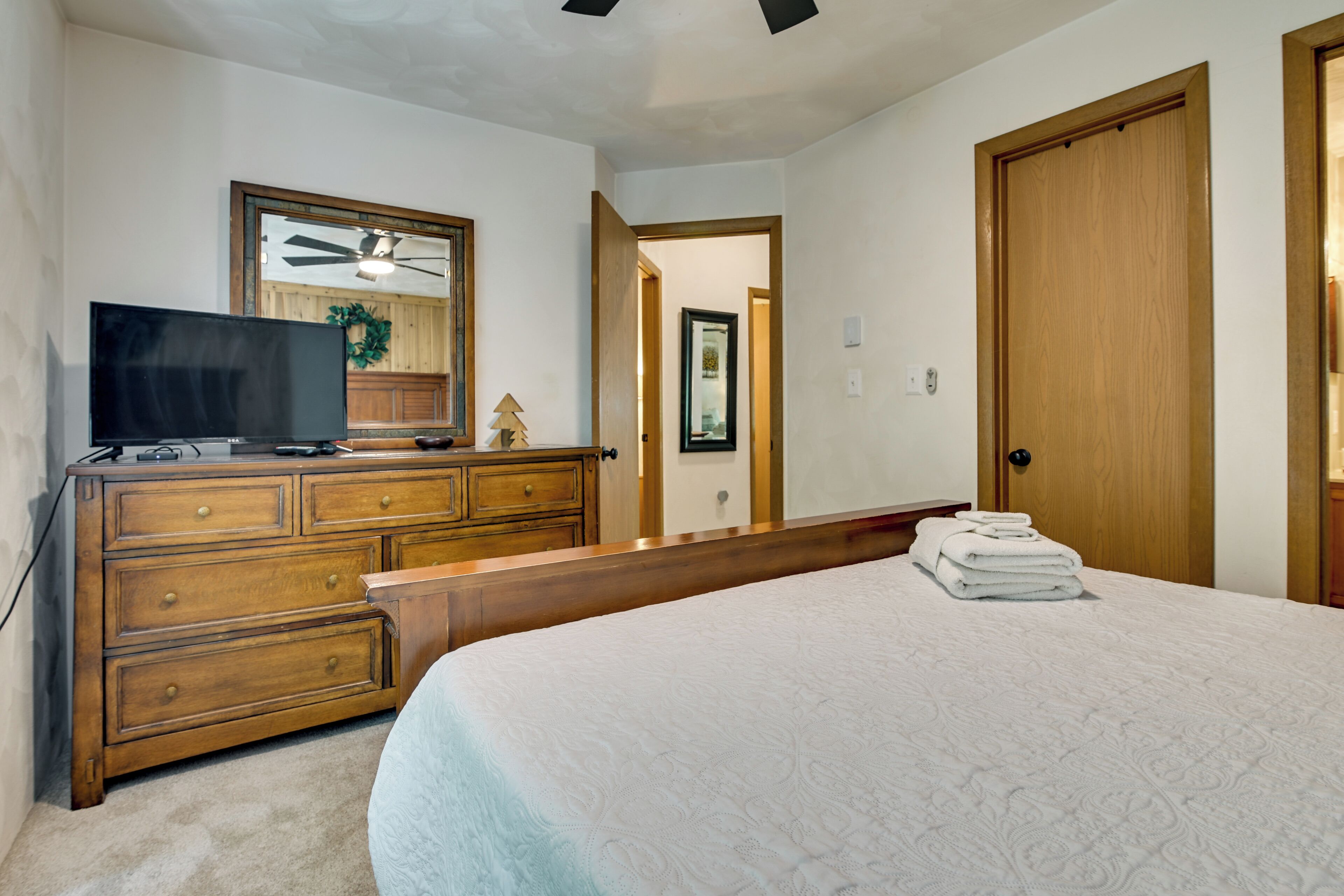 A bedroom with a bed, dresser, television, and a door leading to another room.
