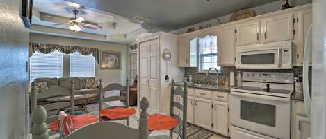 A kitchen with white cabinets, a microwave, an oven, and a ceiling fan.