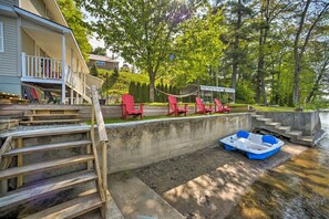 A waterfront property with a dock, red Adirondack chairs, and a boat.