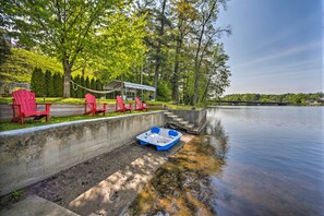 Un cadre idyllique au bord du lac, avec des chaises Adirondack rouges, un espace salon abrité et un petit bateau bleu amarré près de l’eau.