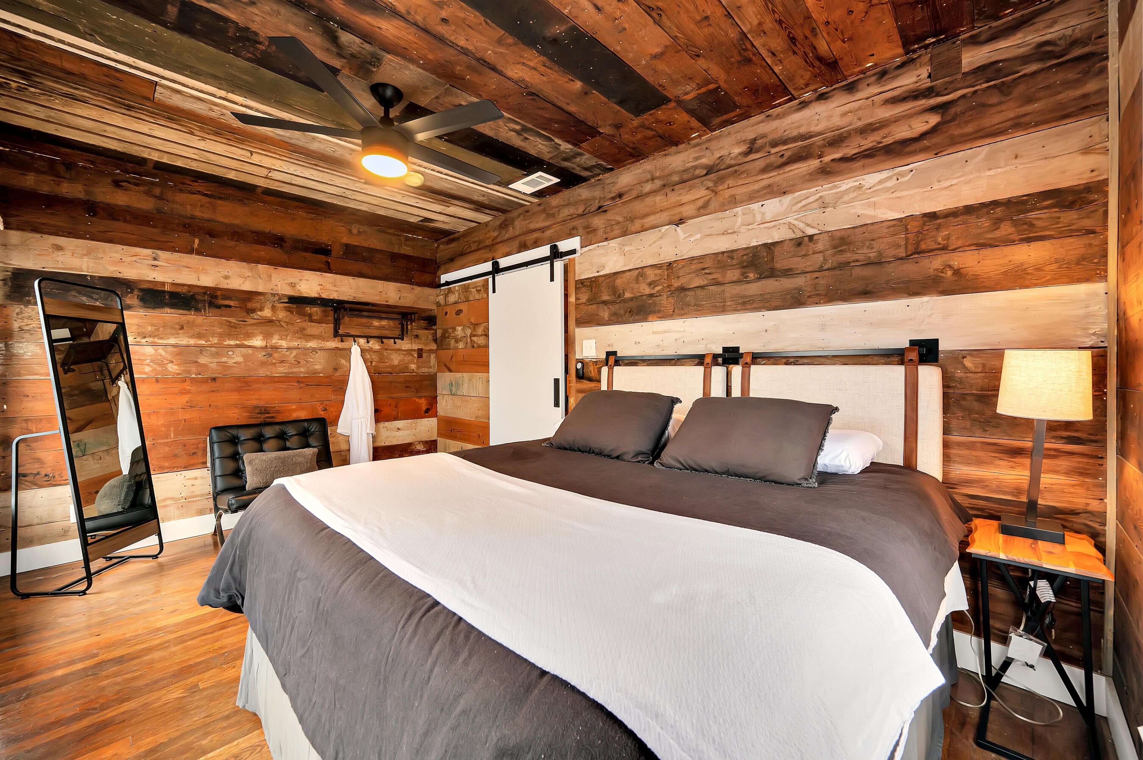 A wooden-paneled bedroom with a large bed, a hanging chair, and a mirror.