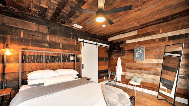 Ein Schlafzimmer mit Holzwandverkleidung, einem Bett, einem stehenden Spiegel und einer Wandleuchte.