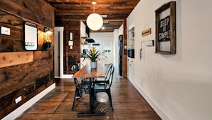 Ein Holzinterieur mit einem Esstisch und Stühlen, einer Pendelleuchte und einer Tür zu einem anderen Raum.