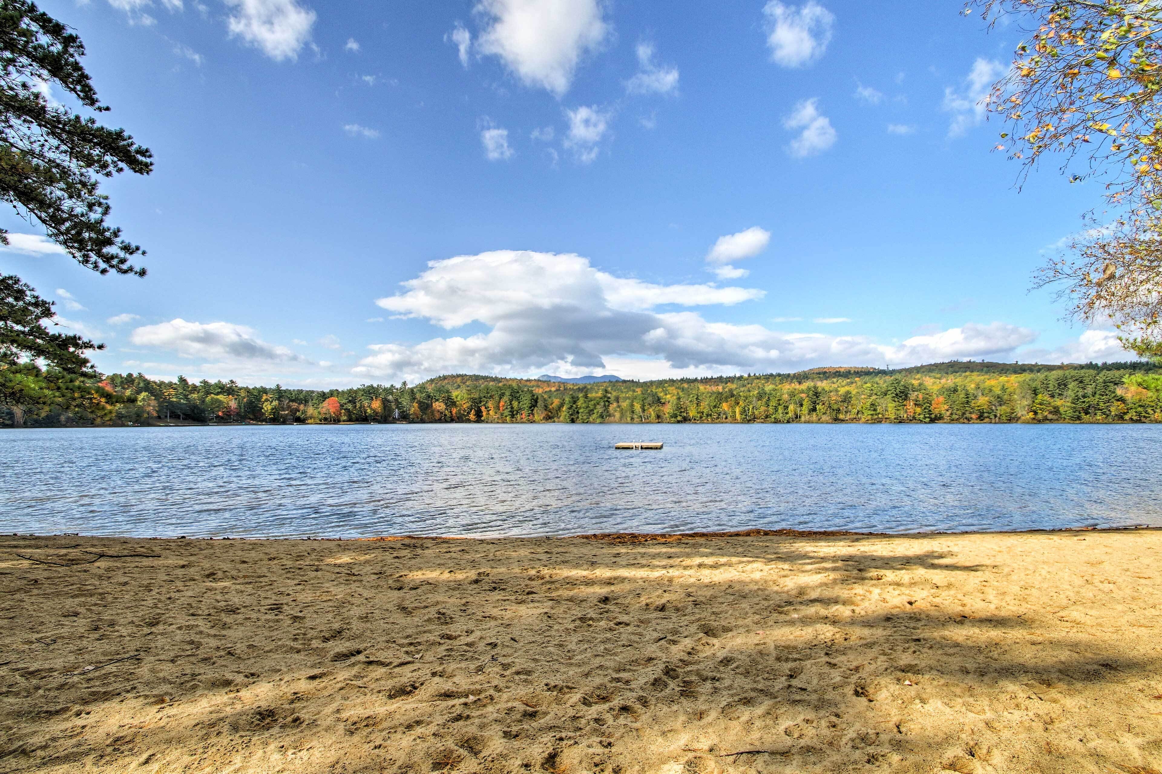 A sandy beach with a lake and forested hills in the background.