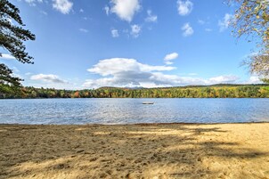 A sandy beach with a lake and forested hills in the background.