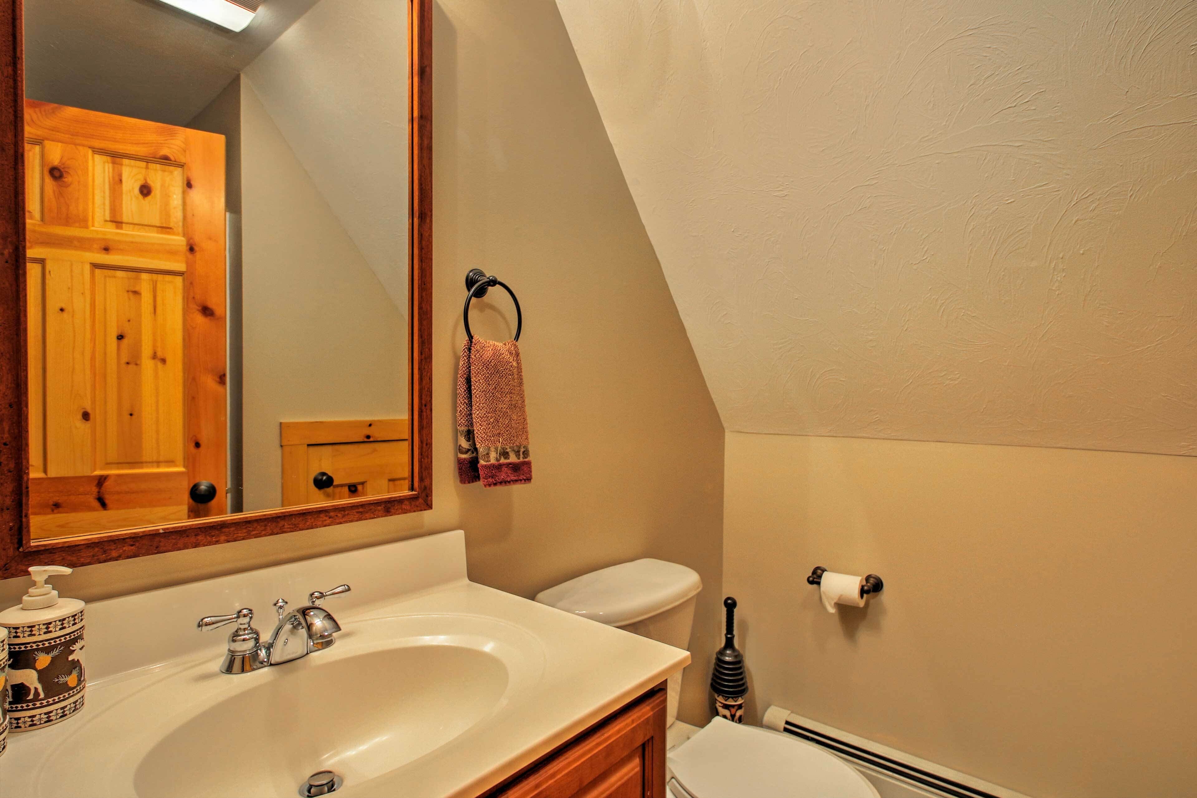Un baño con un mueble de madera, un lavabo con dispensador de jabón, un inodoro y un aro para toallas.