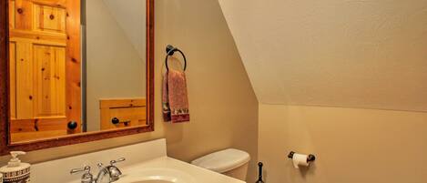 Un baño con un mueble de madera, un lavabo con dispensador de jabón, un inodoro y un aro para toallas.