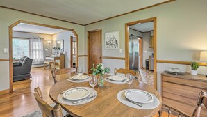 A dining area with a wooden table set for four, surrounded by chairs. There is a kitchen visible in the background, and a living room with a sofa and a window. - Tasteful Country Home on 5 Acres ~ 3 Mi to Lake! (Westmoreland)