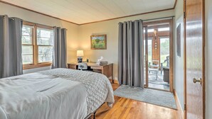 A bedroom with a large bed, a desk with a lamp, and a view of the outdoors through a door. - Tasteful Country Home on 5 Acres ~ 3 Mi to Lake! (Westmoreland)